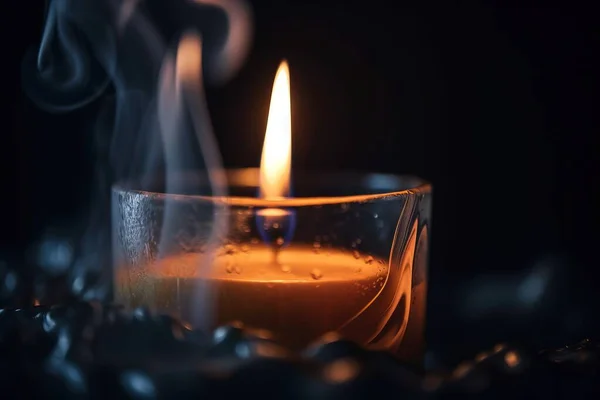 a lit candle in a glass with smoke coming out of it.