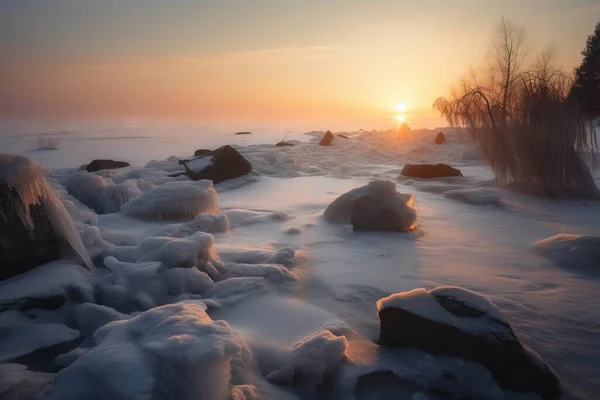 the sun is setting over the water and rocks covered in ice and snow on a frozen lake shore with trees and bushes in the foreground.