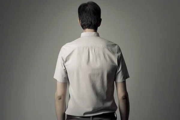 a man in a white shirt is standing back to back with his hands in his pockets and his back turned to the camera and his left.