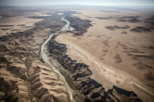an aerial view of a river running through a desert area with sand dunes and mountains in the background and a river running through the middle of the land.