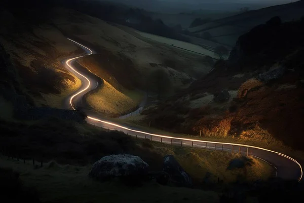 a winding road in the middle of a hilly area with a light trail going down it\'s side in the middle of the night.