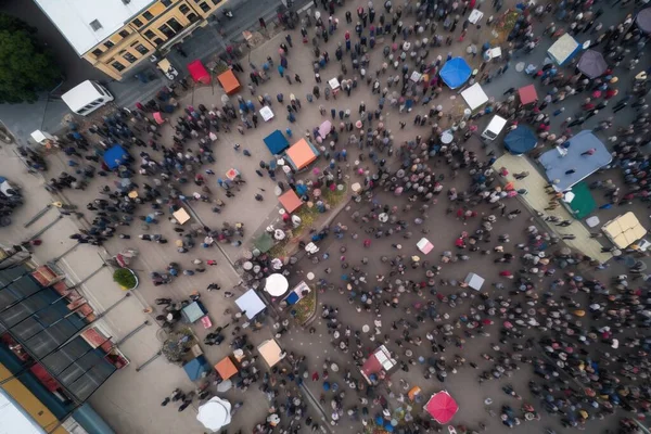 an aerial view of a crowd of people walking around a city square with umbrellas on the sides of the street and buildings in the background.