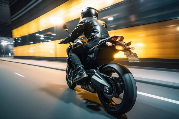 a person riding a motorcycle on a city street at high speed with a blurry background of a building and a yellow light in the background.