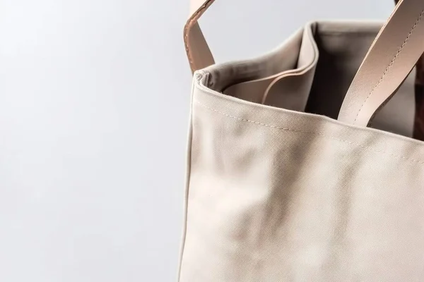 a beige leather bag with two handles and a zippered closure on the inside of the bag, with a brown leather handle, and a white background.