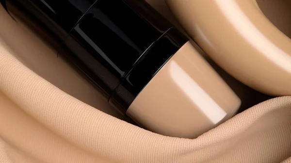 a close up of a tube of foundation cream on a cloth with a beige cloth around it and a black tube of foundation cream on the top of the tube.
