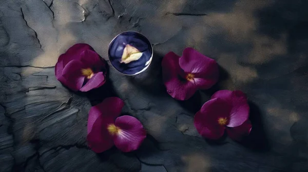 purple flowers are in a bowl on a rock surface with a small bowl of petals in the middle of the picture and a few petals in the middle of the bowl.