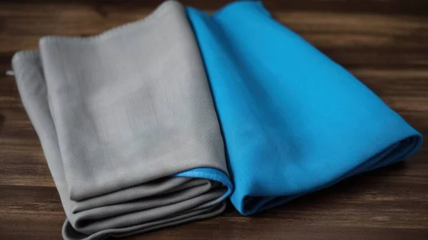 a close up of two different colored cloths on a wooden table with one folded up and the other folded down on a table top.