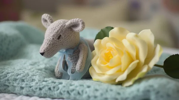 a crocheted teddy bear sitting next to a yellow rose.