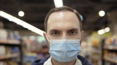 Tired caucasian man wearing mask in a supermarket. looks at the camera. Close-up shot. Pandemic COVID-19.