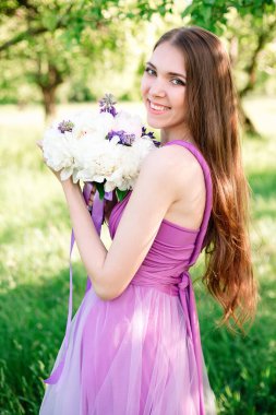 Portrait of a young girl in a light purple dress with a bouquet of peonies in her hands. Graduation, bridesmaid posing in the garden. High quality shot.
