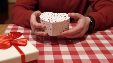 Young man holds in his hands a gift box of red and white color with a surprise inside. The concept of a romantic event on Valentines Day or an anniversary. Close-up high quality 4k footage.