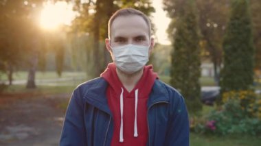 Portrait of a young man in a protective medical mask in a public place. Anti-Covid restrictions in the park. 3840x2160p ultra HD.