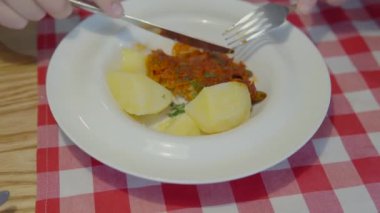 The mans hands cut off a piece of white stewed fish with a knife and take a piece with a fork. Dish with boiled potatoes for lunch, homemade food. Close-up view.