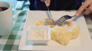 A man eats homemade fish and mashed potatoes with tartar sauce with a knife and fork sitting in a restaurant. Close-up, business lunch on a white plate.