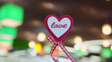 Festive heart-shaped decor, toy, Valentines Day attribute on a stick with a bow and the word love against the colorful vibrant blurred background indoors. Close-up shot, 4k footage.