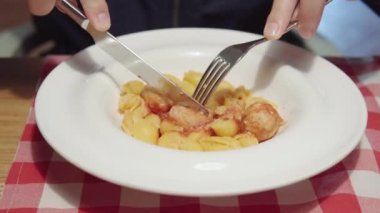 Close-up shot of a visitor eats pasta with chicken meatballs and tomato sauce in restaurant.