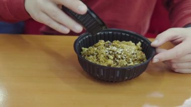 A man pours sweet chili sauce into an Asian dish: rice with vegetables and curry chicken. Food in plastic non-eco-friendly dishes for lunch in a restaurant or at home. Food delivery. Close-up view.
