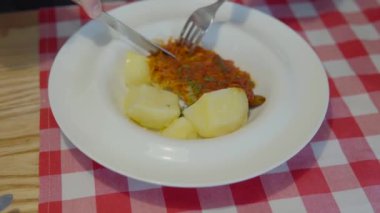 Fish dish for lunch break: a mans hands eat stewed hake or pollock with boiled potatoes with a fork and knife. Close-up view.