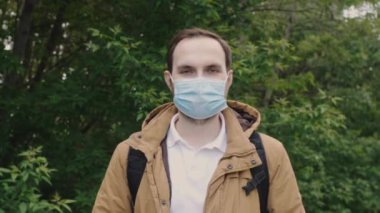 Portrait of a man in a medical protective mask looks into the camera with a positive attitude. Tourist, student, freelancer during covid-19 pandemic.