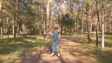 Little girl is rollerblading in the park, her old grandfather is holding her hand.