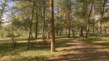 The old man runs funny in the park. In his hand is a walking stick. The girl is rollerblading.