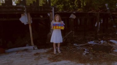 Elinde poster olan bir kız çocukları korumak istiyor. Savaştan kalma yanmış bir evin arka planına karşı..