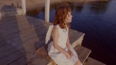 Suyun kenarında kanatları olan tatlı küçük bir melek kız ve romantik olarak sıkılmış..