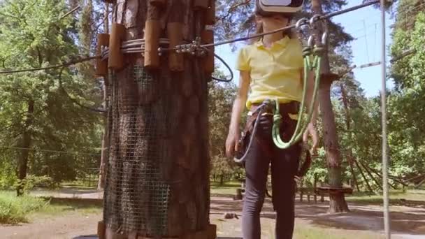 这个女孩玩一个虚拟游戏 她实际上是去参加体育活动 虚拟现实眼镜有助于体育运动 虚拟眼镜沉浸在孩子们的森林绳索探险公园里 — 图库视频影像