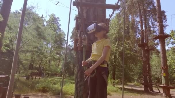 这个女孩玩一个虚拟游戏 她实际上是去参加体育活动 虚拟现实眼镜有助于体育运动 虚拟眼镜沉浸在孩子们的森林绳索探险公园里 — 图库视频影像