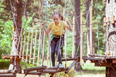 İplerden yapılmış bir orman macera parkındaki çocuk. Çocukların açık hava tırmanış eğlence merkezi. Çocuklar için oyun alanı ve kablolu spor. Spor askıya alınmış halat eğitmeni.