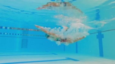 Kadın sporcu havuzda su altında yüzer. Antrenman sırasında havuzda bir kadın yüzücünün yavaş hareketi. Yüzücü derin sulara dalıyor..