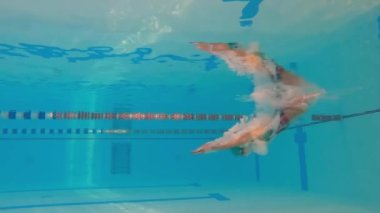 Kadın sporcu havuzda su altında yüzer. Antrenman sırasında havuzda bir kadın yüzücünün yavaş hareketi. Yüzücü derin sulara dalıyor..