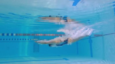 Kadın sporcu havuzda su altında yüzer. Antrenman sırasında havuzda bir kadın yüzücünün yavaş hareketi. Yüzücü derin sulara dalıyor..