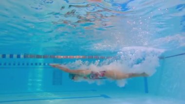 Kadın sporcu havuzda su altında yüzer. Antrenman sırasında havuzda bir kadın yüzücünün yavaş hareketi. Yüzücü derin sulara dalıyor..