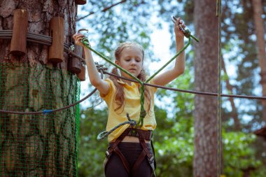 İplerden yapılmış bir orman macera parkındaki çocuk. Çocukların açık hava tırmanış eğlence merkezi. Çocuklar için oyun alanı ve kablolu spor. Spor askıya alınmış halat eğitmeni.
