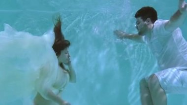 Bir kadın ve bir adam suyun altında yüzüyorlar. Bir kadın bir erkeği suyun altında öper..