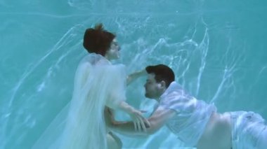 Bir kadın ve bir adam suyun altında yüzüyorlar. Bir kadın bir erkeği suyun altında öper..