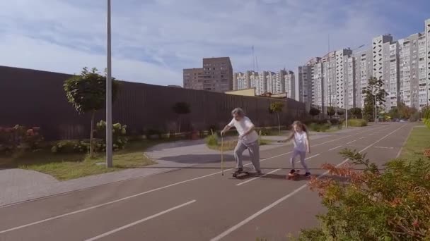 小女孩教一个老人骑滑板 他们正在训练如何在街上玩滑板 爷爷正骑着滑板 — 图库视频影像