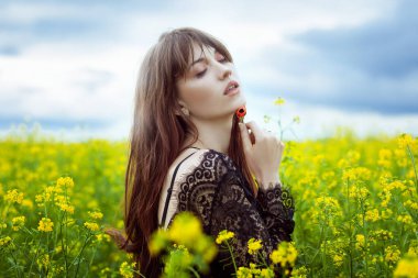 Genç ve güzel bir kadın sarı çiçeklerle dolu bir tarlada duruyor ve üzgün. Güzel bir kadının üzgün yüzü..