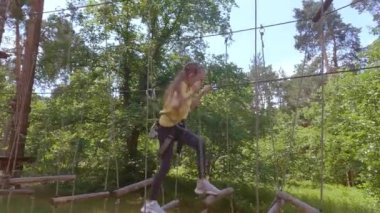İplerden yapılmış orman macera parkında bir çocuk. Kız yüksek bir iple yola tırmanıyor. Çocukların açık hava tırmanış eğlence merkezi. Çocuklar için oyun alanı ve teleferikli spor.