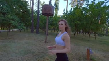 Parkta koşan atletik bir kadın kardiyo antrenmanı yapıyor. Ağır yüklerden önce koşmak bir ısınmadır. Parkta dışarıda koşmak kadınlar için yararlıdır..