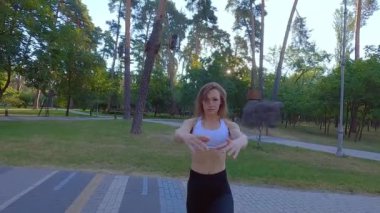 Parktaki spor antrenmanından önce ısınan bir kadın. Spor malzemesi olarak parkta bir bank..