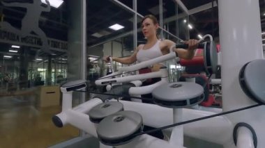 Spor salonundaki kadın vücut geliştirme makineleriyle antrenman yapıyor. Bir kadın kaslarını simülatöre pompalıyor. Kadın vücudunu spor makinesinde çalıştırmak.