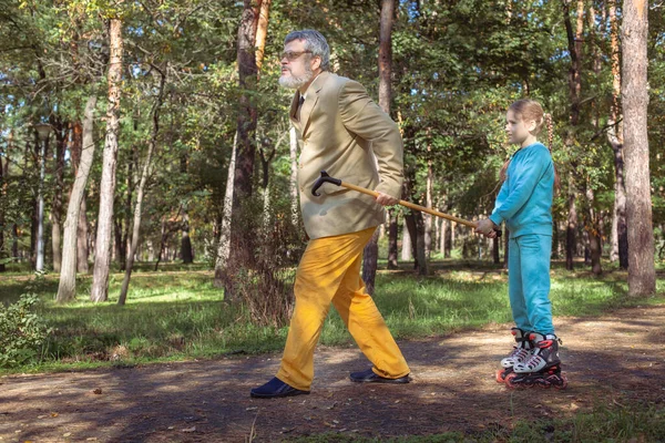Grootvader Loopt Met Zijn Kleindochter Het Park Een Meisje Rolschaatst Rechtenvrije Stockafbeeldingen