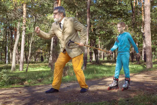 Grootvader Loopt Met Zijn Kleindochter Het Park Een Meisje Rolschaatst Stockafbeelding