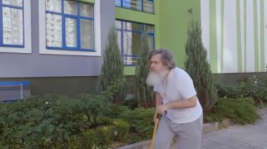 Yaşlı büyükbabam sokağın aşağısında kaykay sürüyor. Yaşlı adam kaykaya binmek için bastona yardım ediyor. Yaşlı bir adam kaykay sürmeyi öğreniyor..