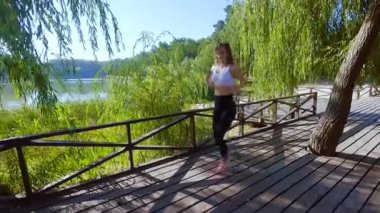 Parkta koşan atletik bir kadın kardiyo antrenmanı yapıyor. Ağır yüklerden önce koşmak bir ısınmadır. Parkta dışarıda koşmak kadınlar için yararlıdır..