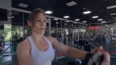 Spor salonundaki kadın vücut geliştirme makineleriyle antrenman yapıyor. Bir kadın kaslarını simülatöre pompalıyor. Kadın vücudunu spor makinesinde çalıştırmak.