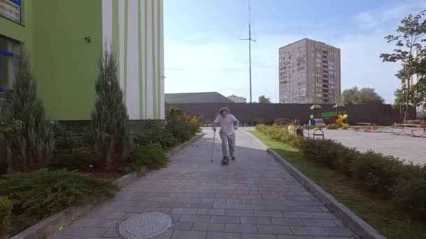 老爷爷在街上骑滑板 那位老人用手杖帮助他骑滑板 一位老人正在学习骑滑板 — 图库视频影像