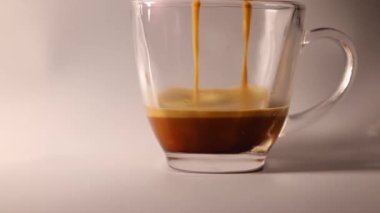 Kahve makinesinden şeffaf bir fincanda kahve akışı, yavaş çekimde.